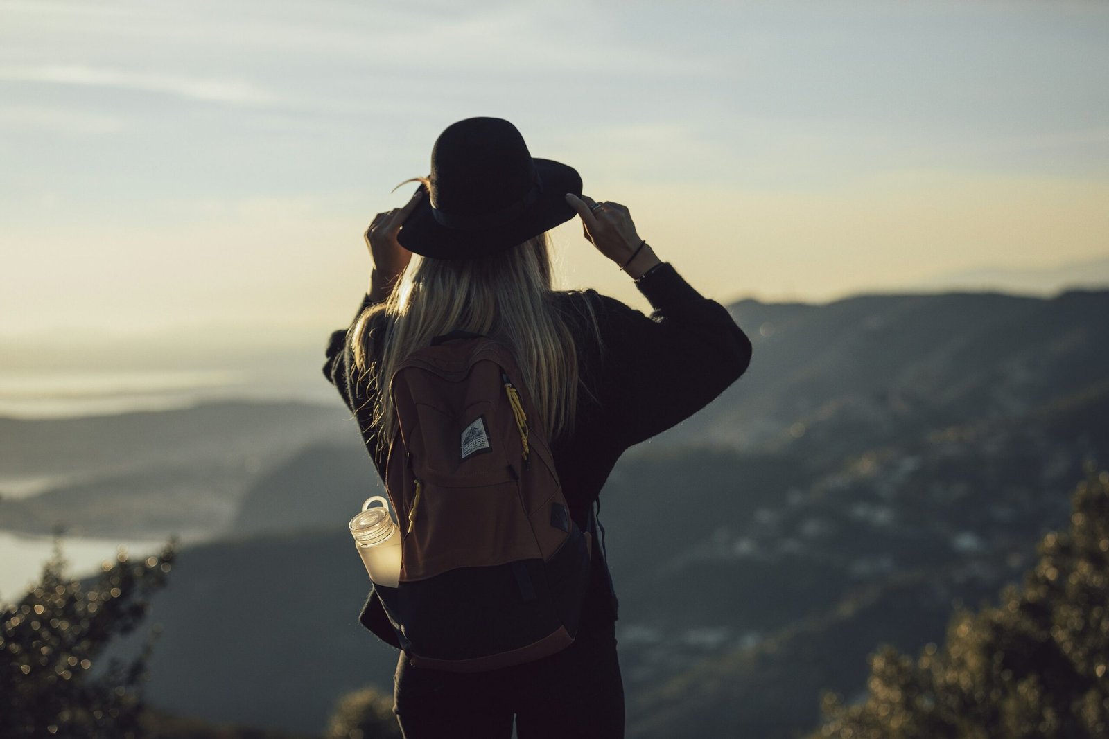 woman in gray hoodie and black pants wearing black hat standing on top of mountain during